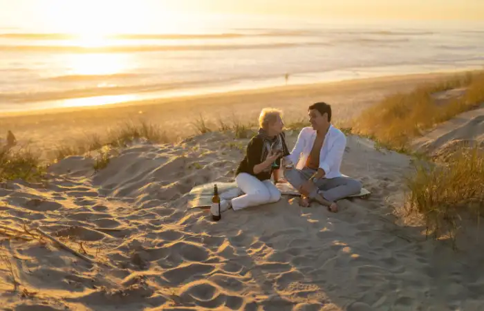 Ein älteres Paar sitzt am Meer in den Dünen und trinkt Wein zusammen