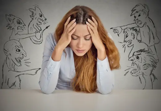 Sich-schuldig-fühlen-ohne-Grund Ein Frau verbirgt ihren Kopf zwischen den Händen, während gezeichnete Figuren auf sie zeigen und sie beschuldigen